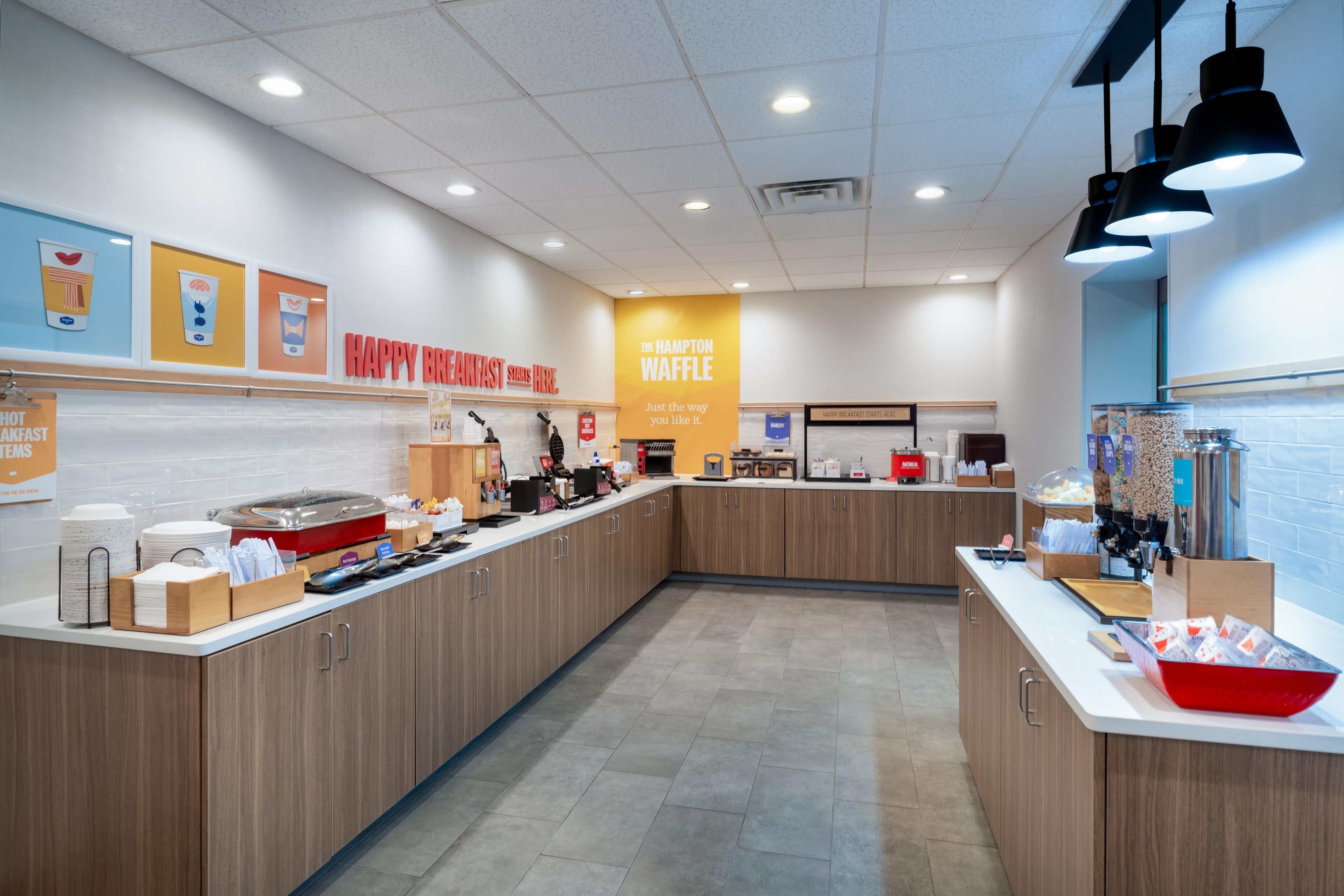 Un espace réservé au petit-déjeuner, comprenant un comptoir, un présentoir pour les aliments et un panneau indiquant le nom « Hampton Waffle ».