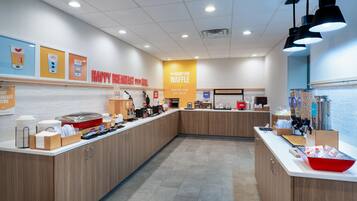 A breakfast area with a counter, food display, and a sign for the Hampton Waffle.