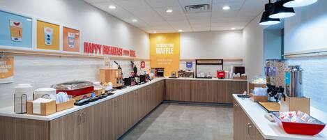 Un espace réservé au petit-déjeuner, comprenant un comptoir, un présentoir pour les aliments et un panneau indiquant le nom « Hampton Waffle ».