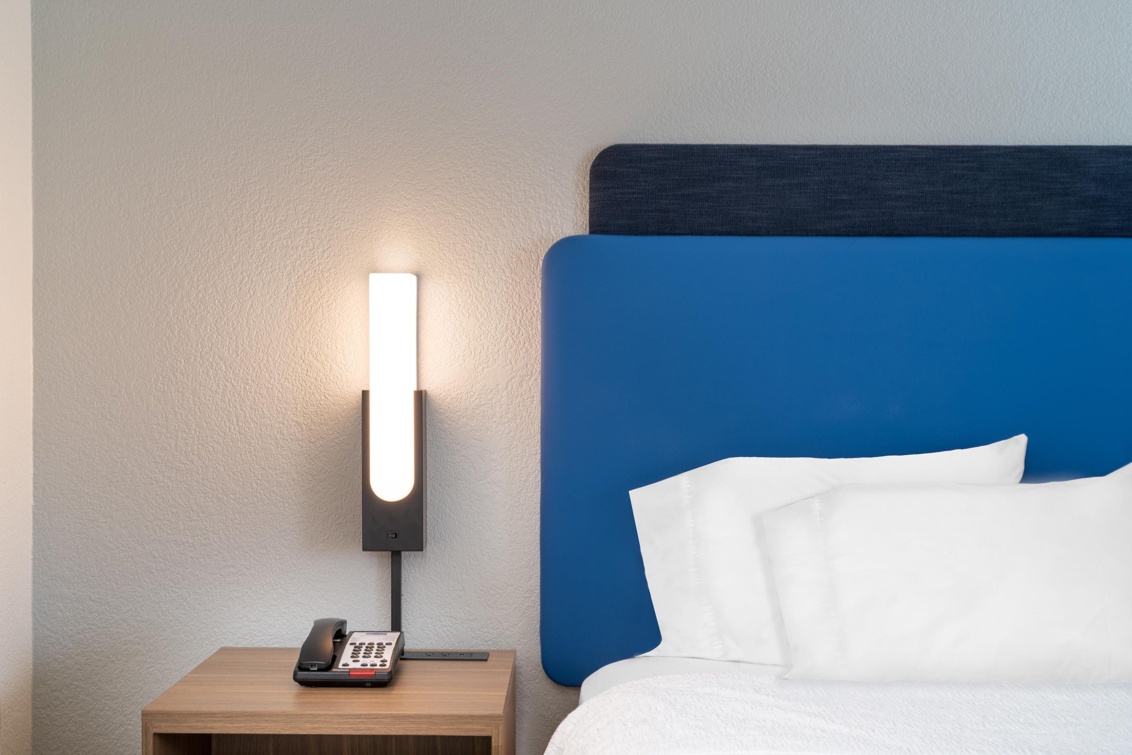 Een hotelkamer met een bed, een nachtkastje met een telefoon en een wandlamp.