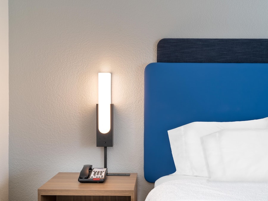 Et hotelværelse med en seng, et sengebord med en telefon og en lampe fastgjort på væggen.