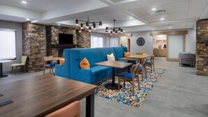A modern lounge area with a blue sofa, wooden tables, and chairs. - Hampton Inn Marietta (Marietta)