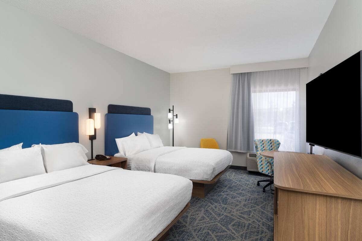 A hotel room with two beds, a desk, a chair, a TV, and a window with curtains.