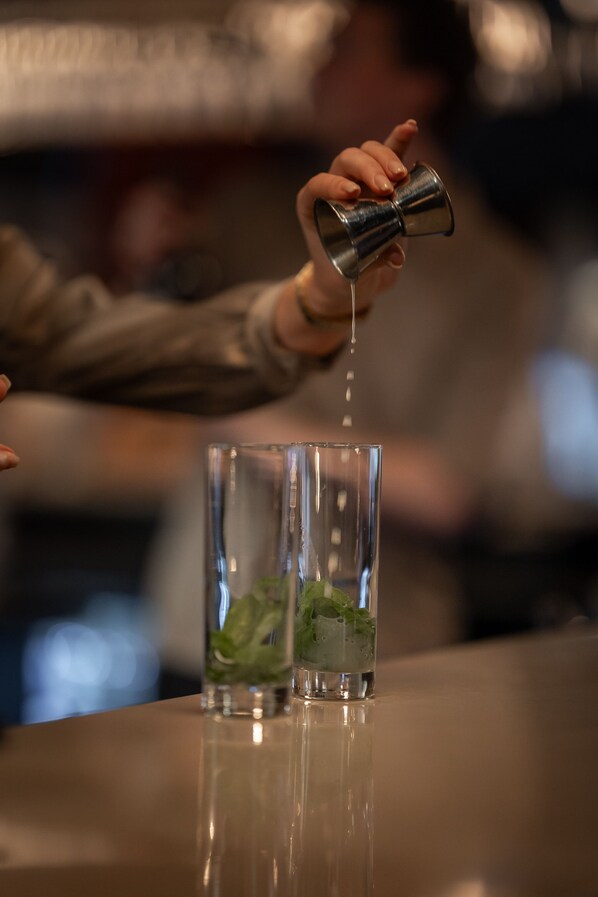 A person pouring a clear liquid into a glass with mint leaves.