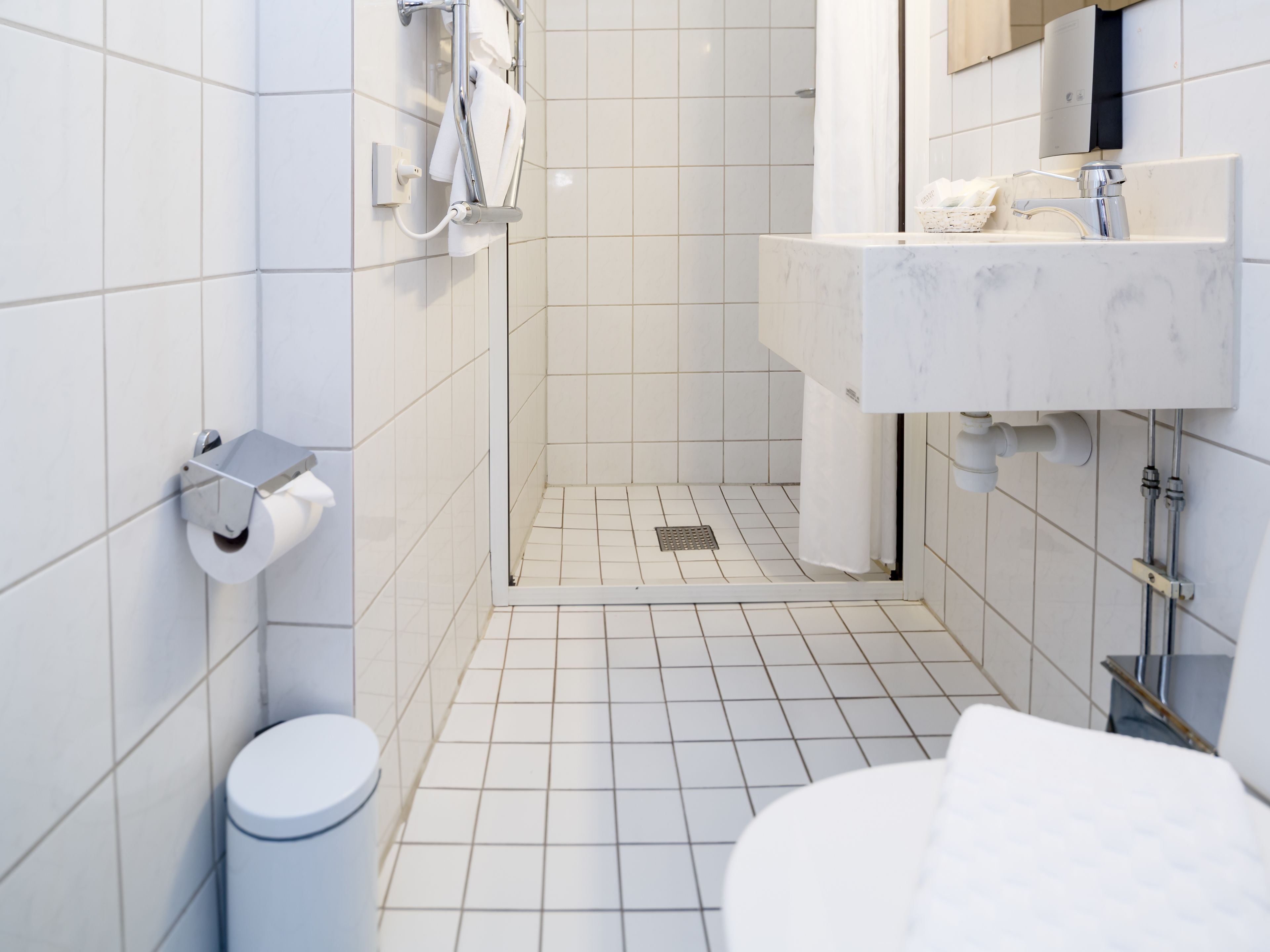 Et moderne badeværelse med hvide fliser, toilet, bruseniche og vask med spejl.