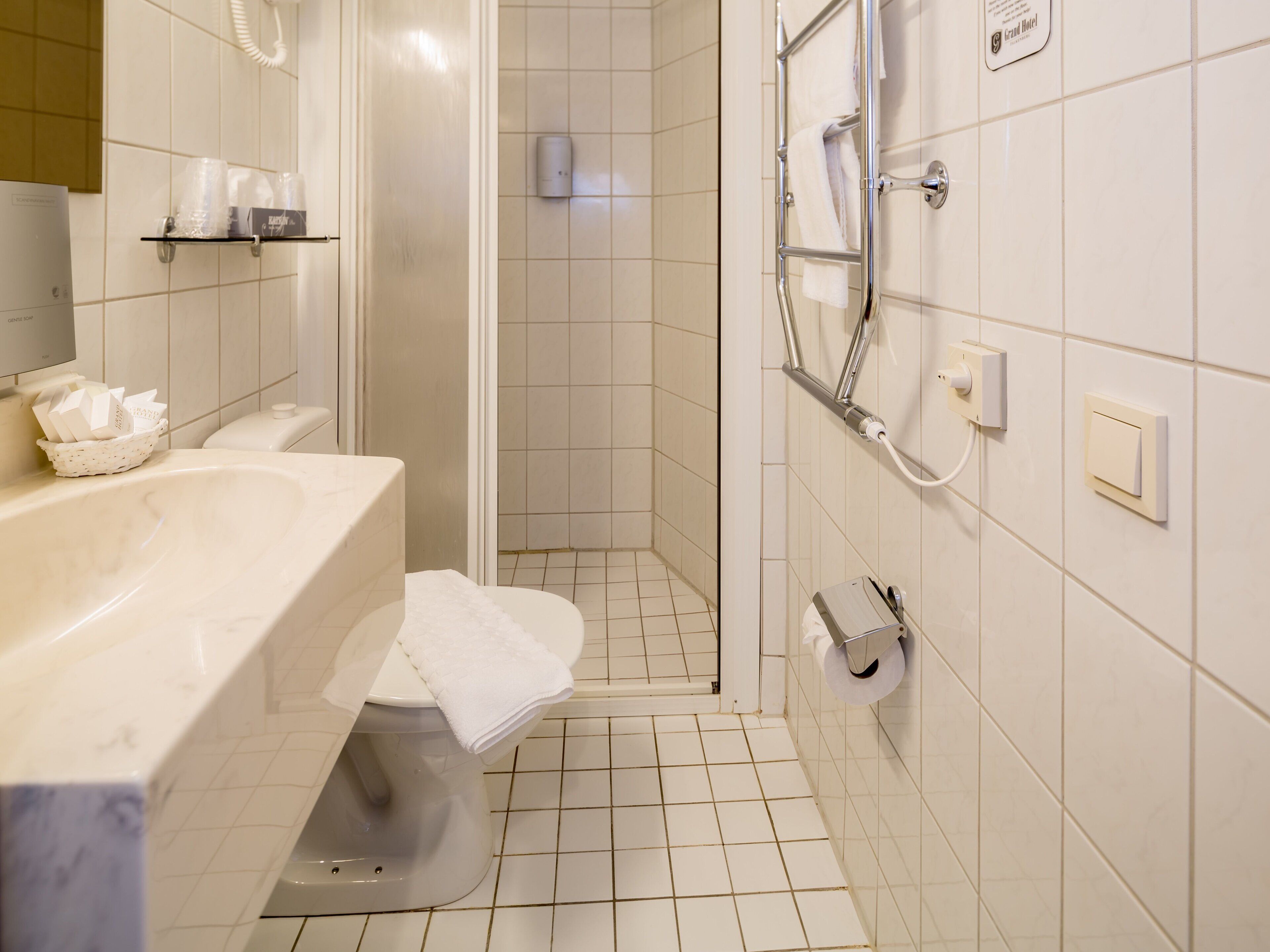 A bathroom with a white sink, toilet, and shower area. There are shelves with toiletries and a towel rack.