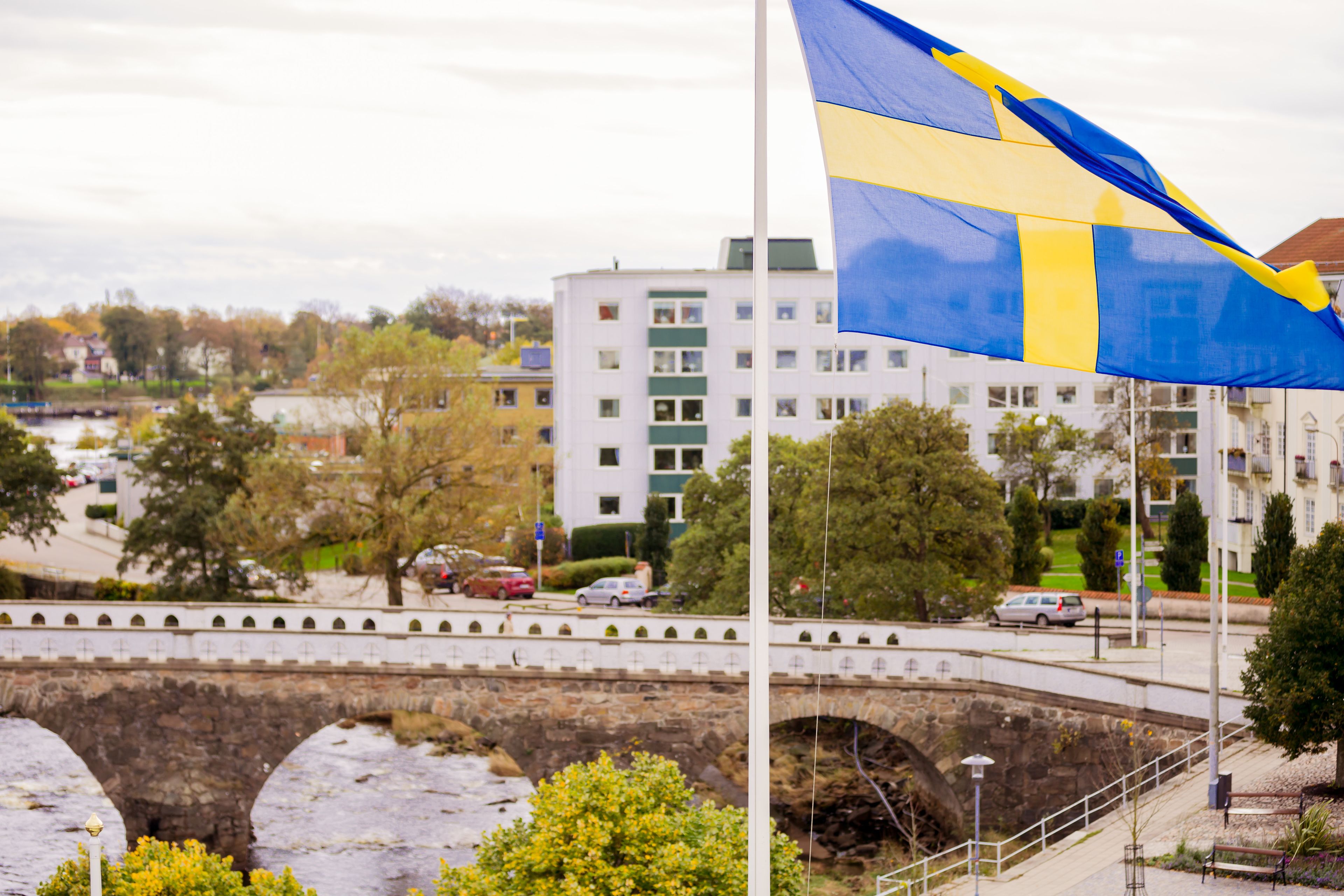 A stone bridge over a river, a flagpole with a flag, and a building in the background.