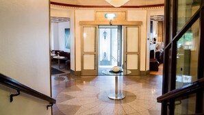 A hotel lobby with a grand chandelier, a glass table with a decorative item, and a door leading to another area.