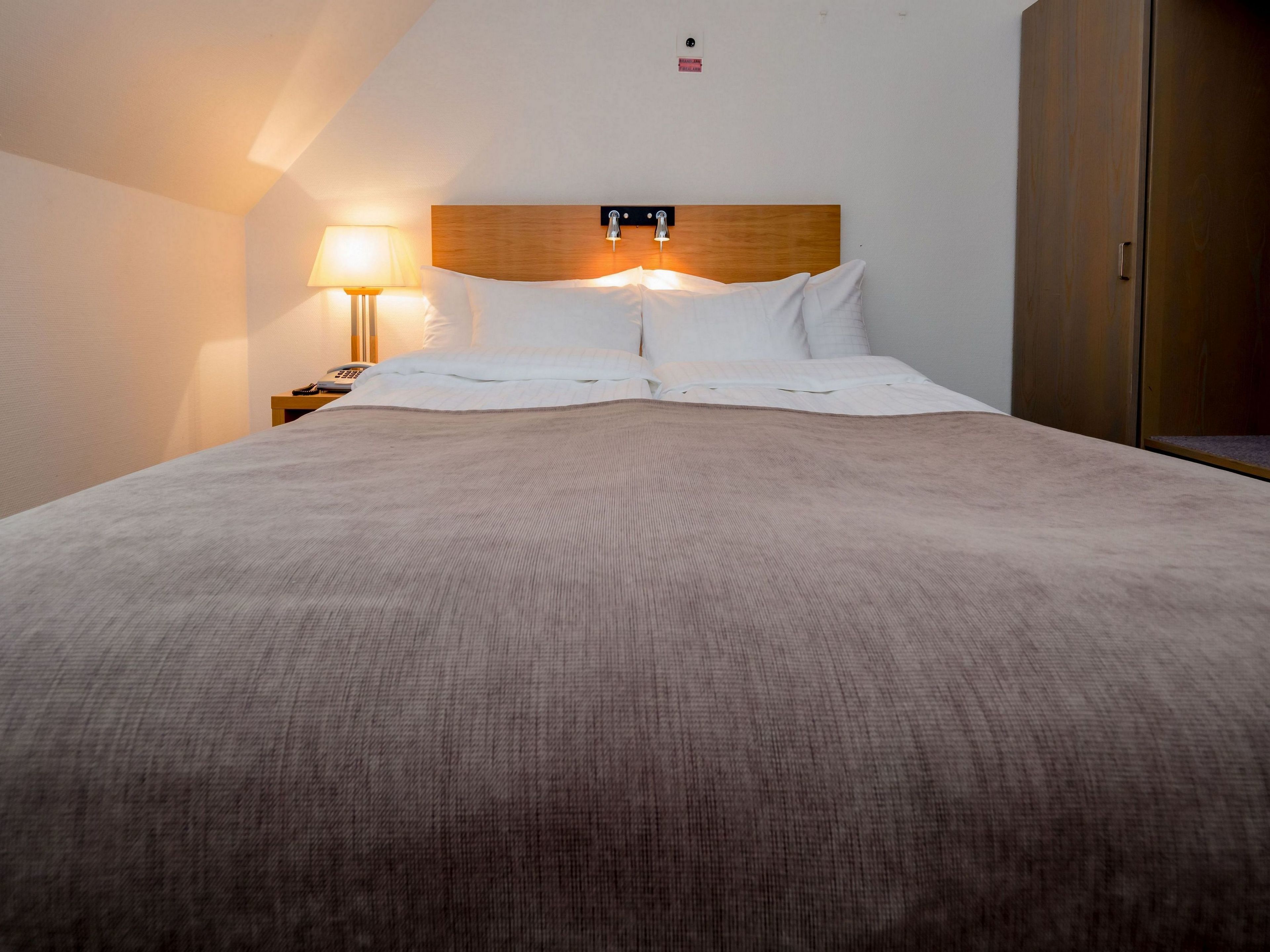 A neatly made bed with a wooden headboard, a bedside lamp, and a wooden wardrobe.