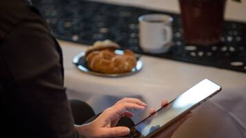 Una persona sosteniendo un teléfono inteligente, con un croissant y una taza sobre una mesa al fondo.