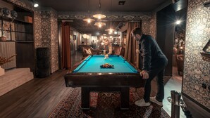 A pool table in a room with patterned wallpaper and wooden flooring.