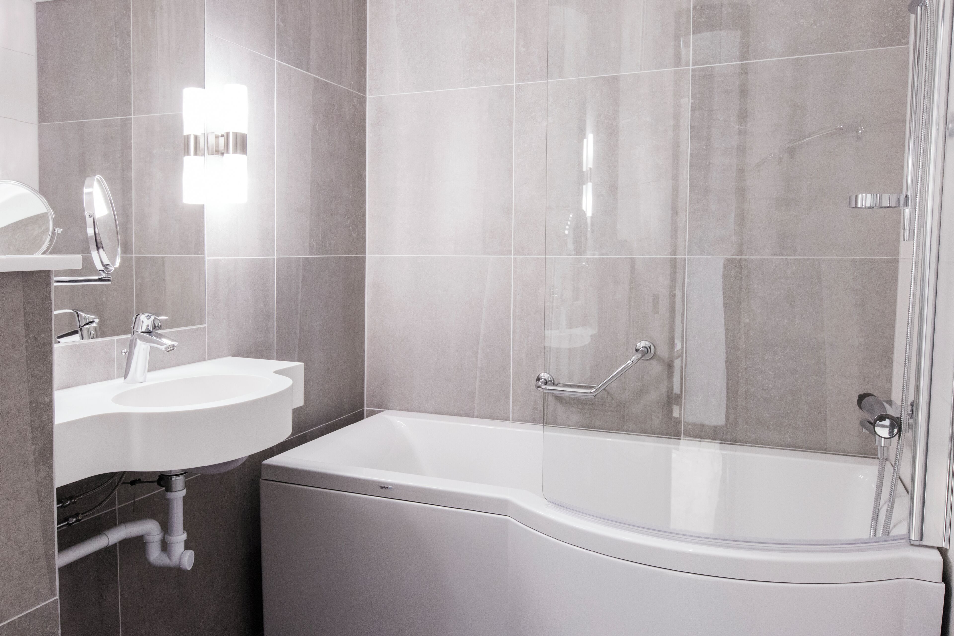 A modern bathroom with a white sink, mirror, and bathtub.