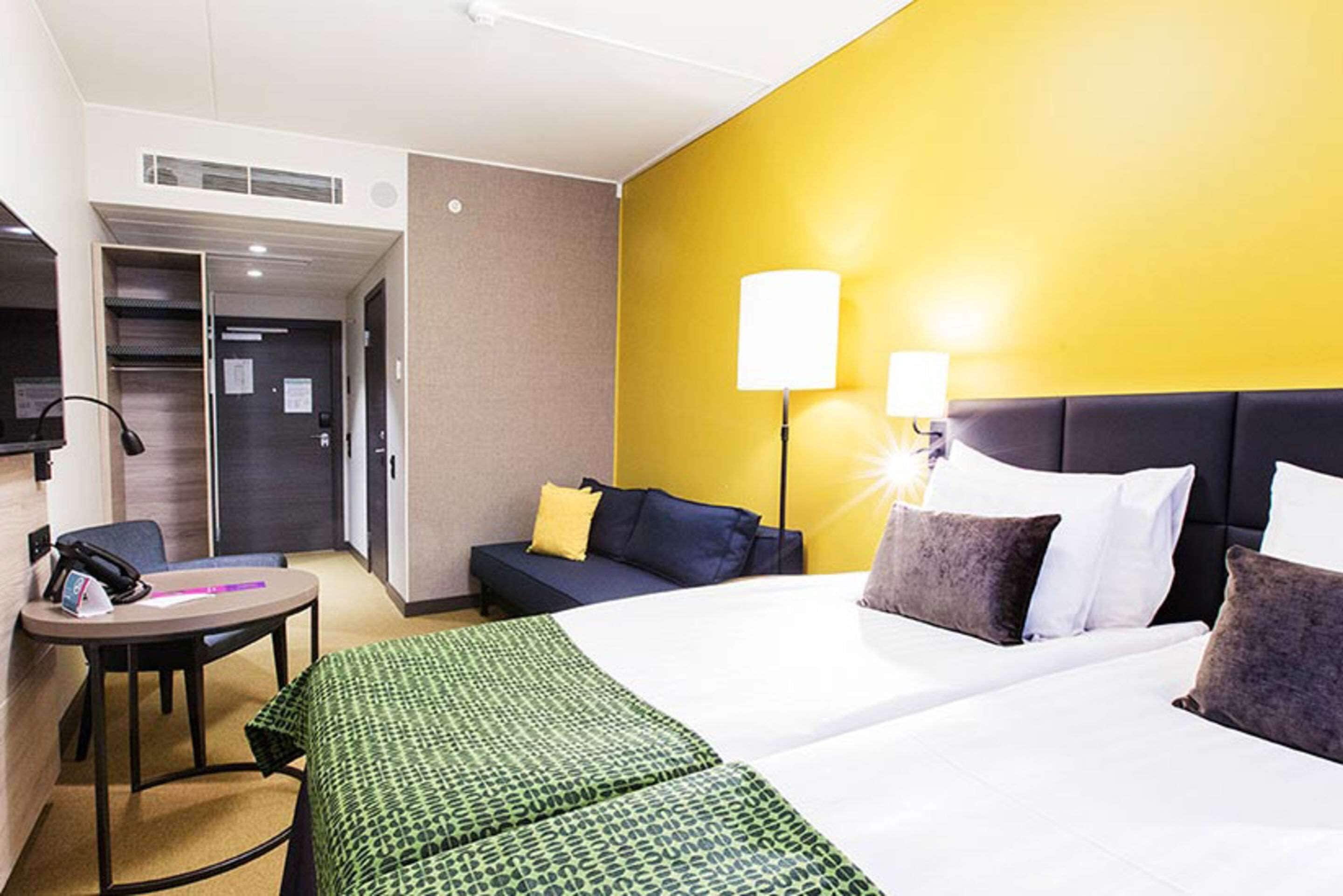 Hotellihuone, jossa on sänky, työpöytä, tuoli, sohva ja kaksi yöpöytävalaisinta.