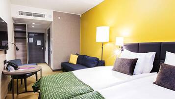Hotellihuone, jossa on sänky, työpöytä, tuoli, sohva ja kaksi yöpöytävalaisinta.