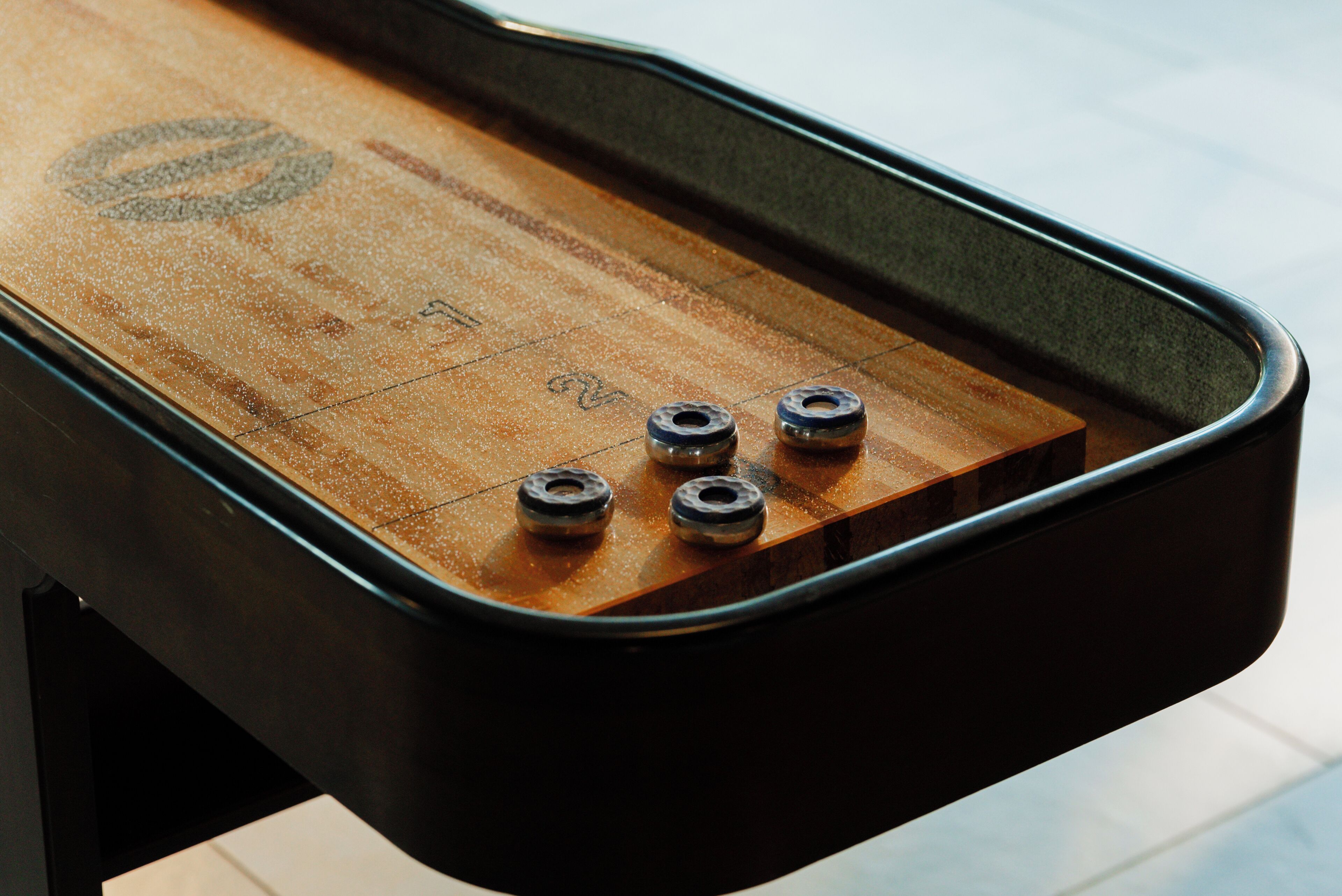 Una mesa de shuffleboard con zonas de puntuación numeradas y discos.