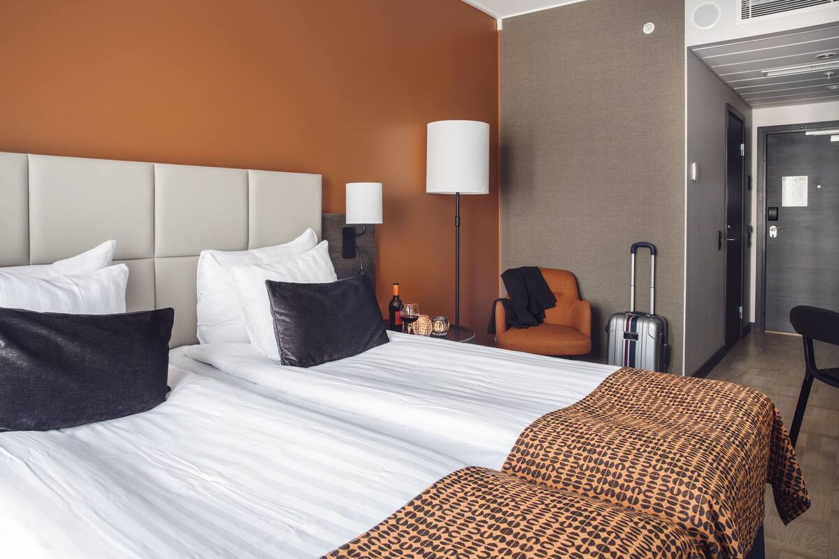 A hotel room with a large bed, a chair, a suitcase, and a lamp.