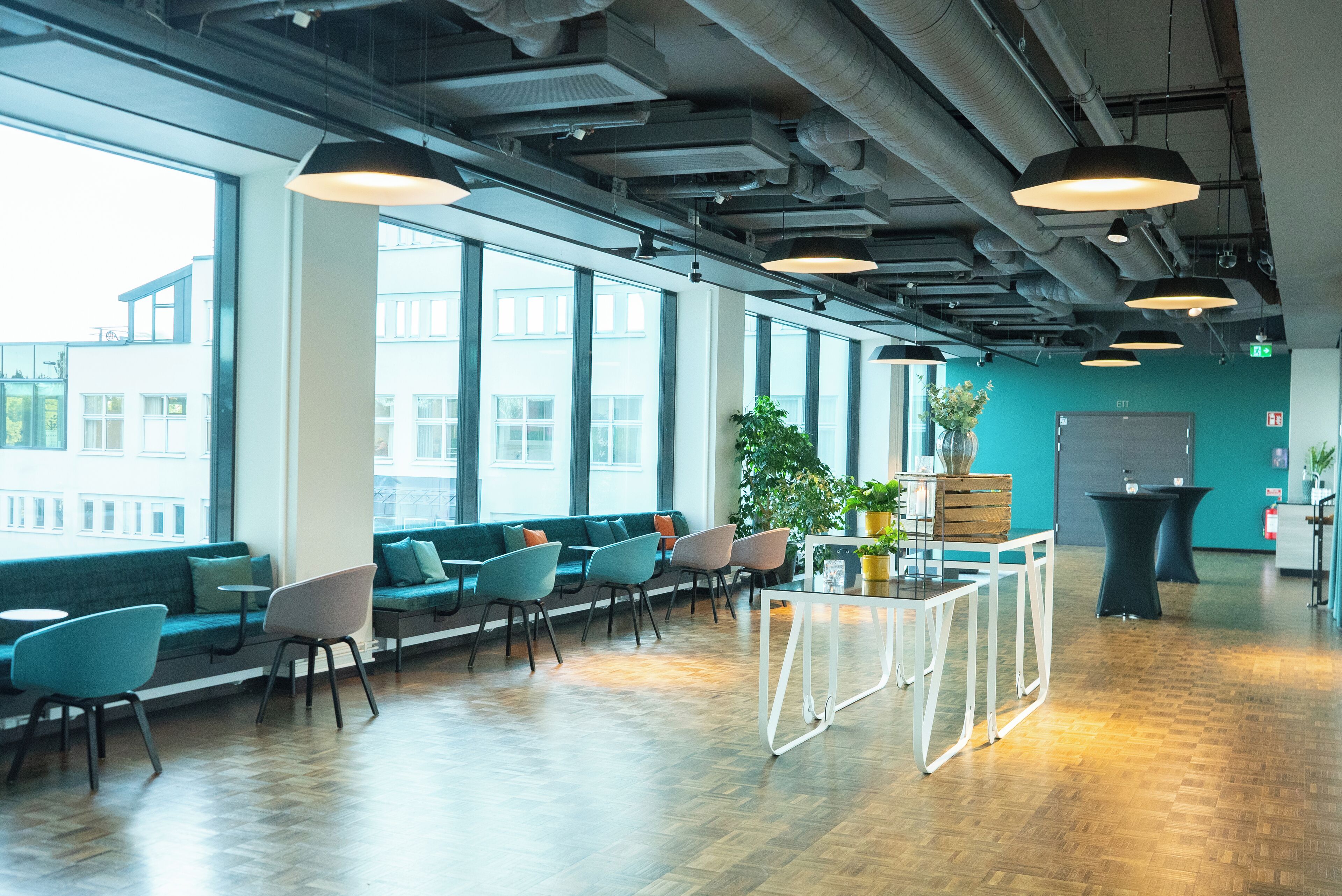 A modern lounge area with seating, large windows, and industrial ceiling elements.