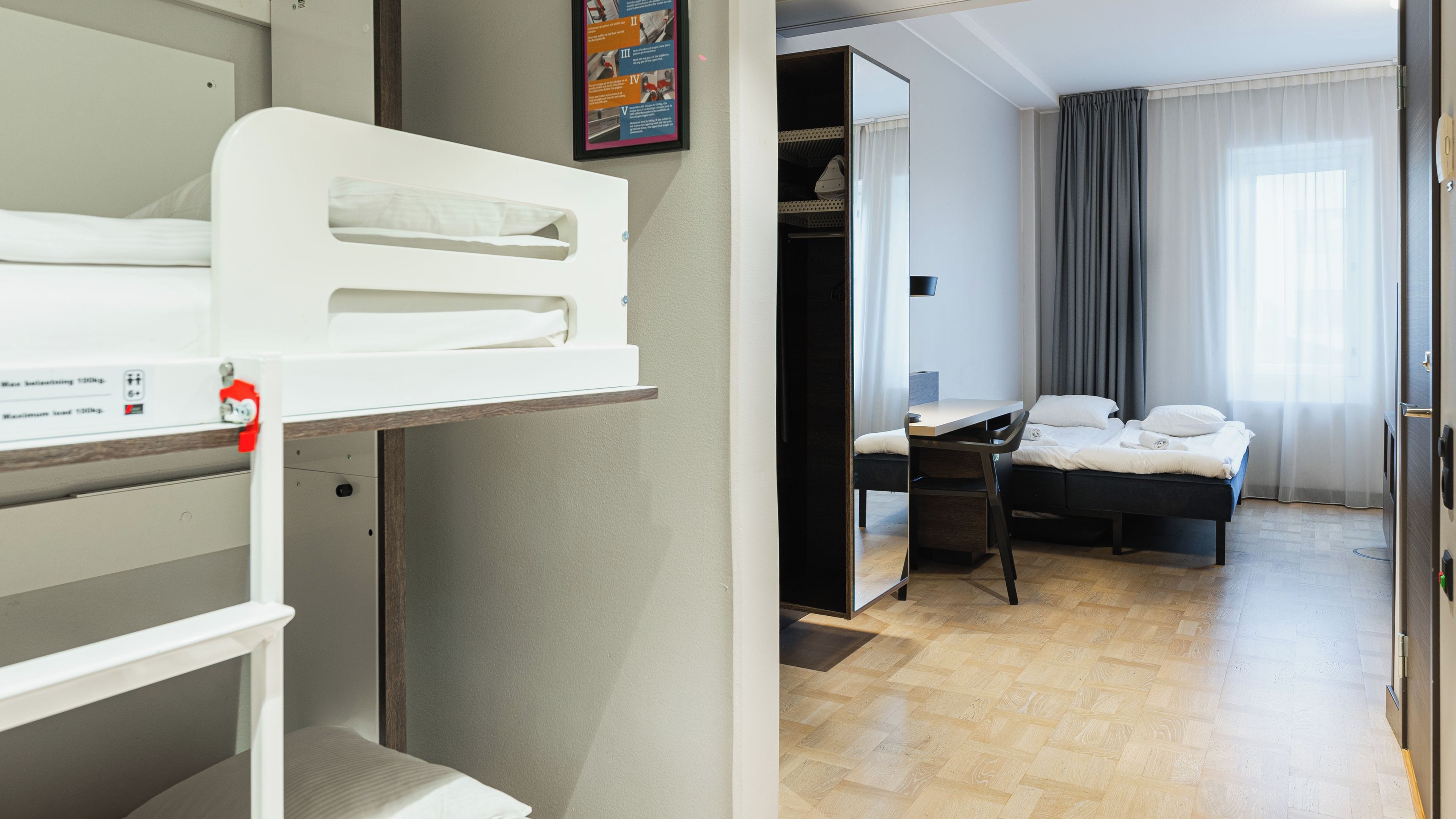 Una habitación de hotel con literas, un escritorio, una silla, una cama y un armario.