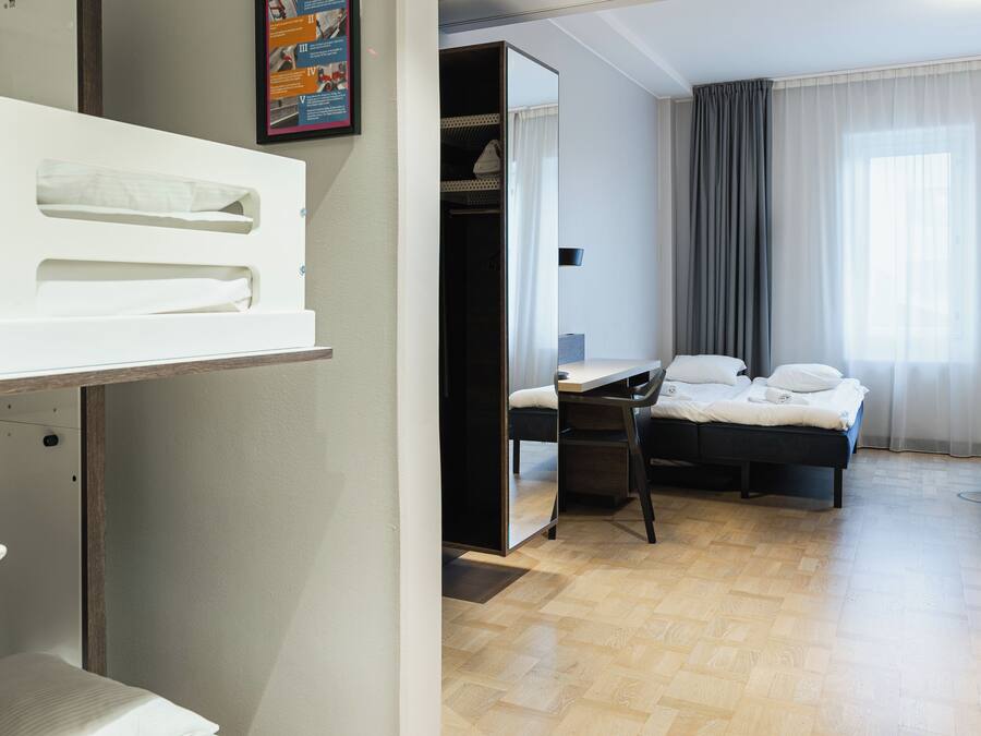 Una habitación de hotel con literas, un escritorio, una silla, una cama y un armario.