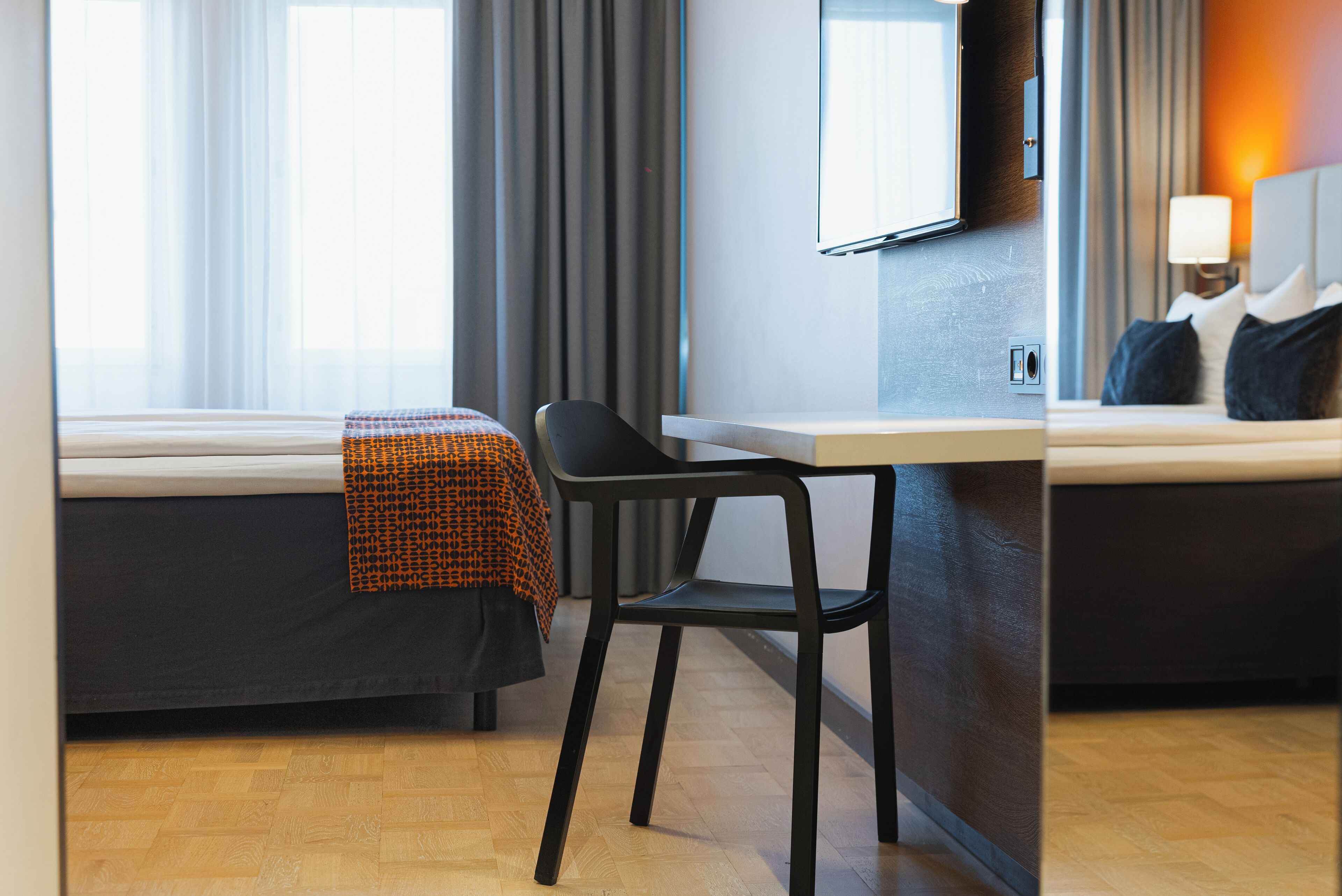 Une chambre d’hôtel avec un lit, un bureau, une chaise, une télévision et une fenêtre avec des rideaux.