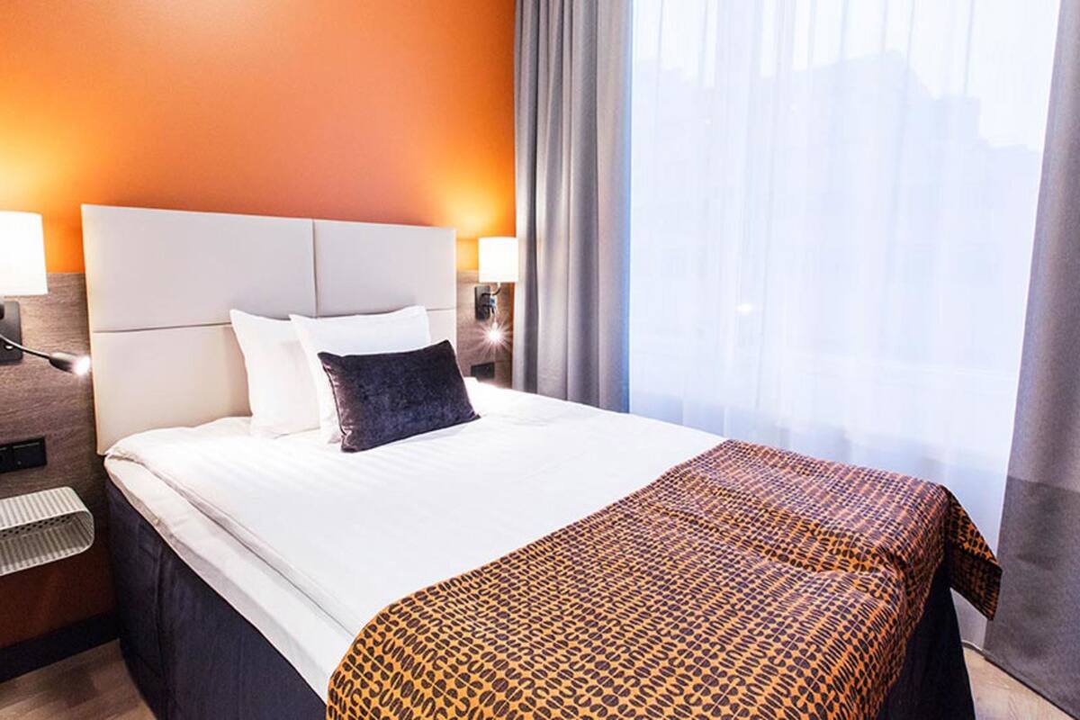 A hotel room with a large bed, a nightstand, a lamp, and a window with curtains.