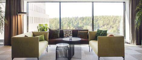 A modern living room with a sofa, two armchairs, a coffee table, and a view of a forest through large windows.