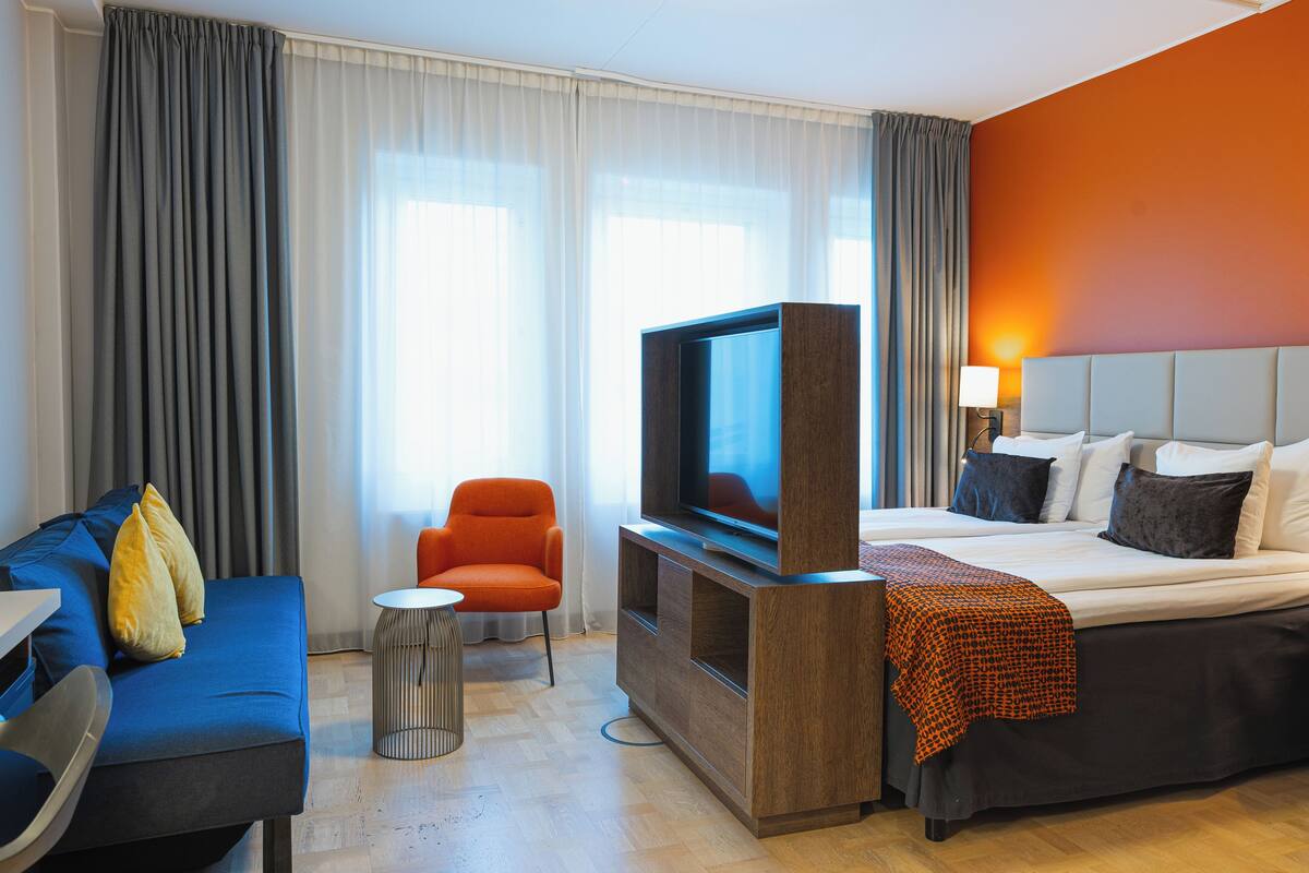 A hotel room with a bed, a TV, a sofa, and a chair.