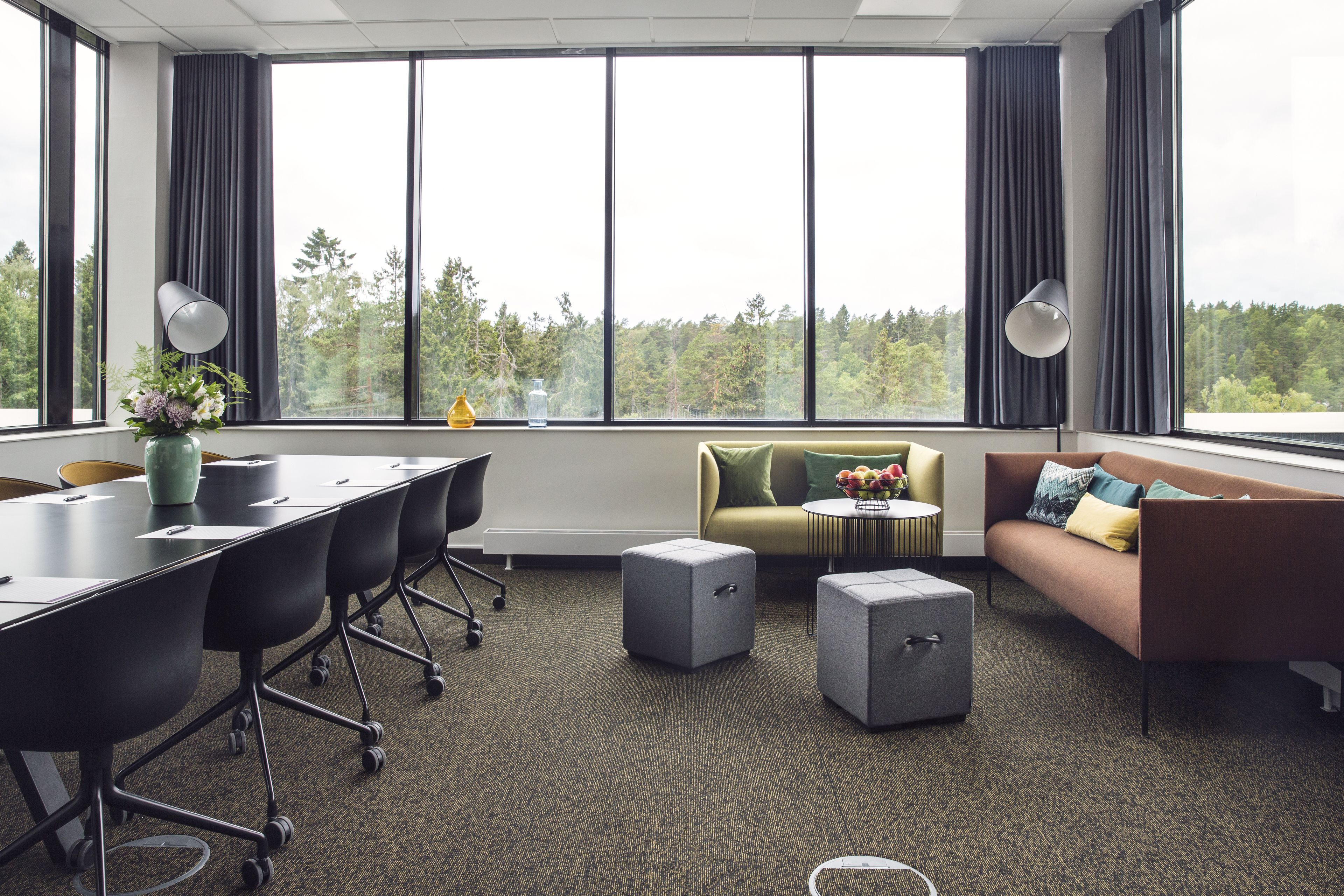 A modern conference room with a long table, black chairs, a sofa, and ottomans.