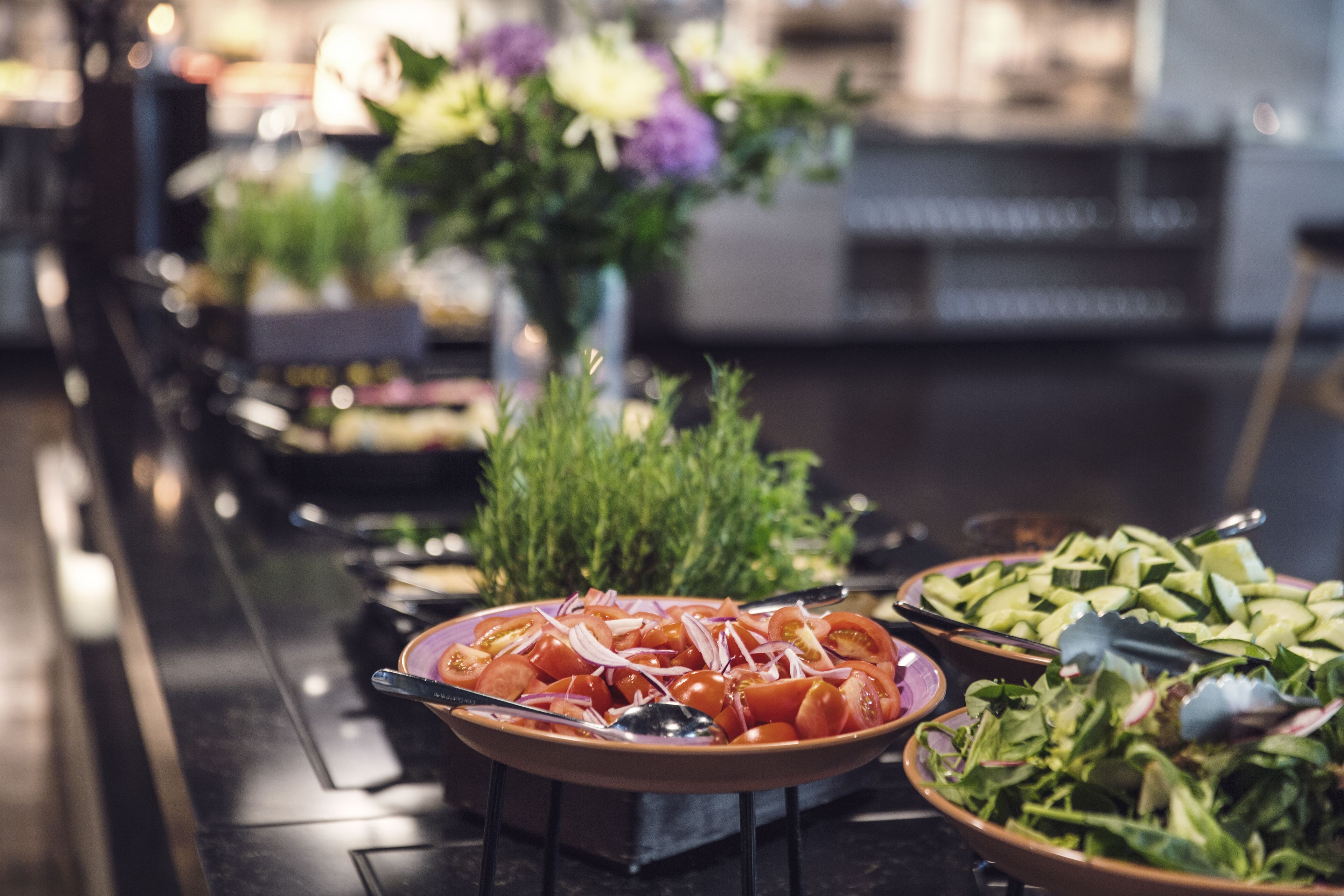 Une table de buffet proposant divers plats, notamment des tomates et des concombres en tranches, ainsi qu’une salade.