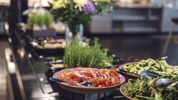 Une table de buffet proposant divers plats, notamment des tomates et des concombres en tranches, ainsi qu’une salade.