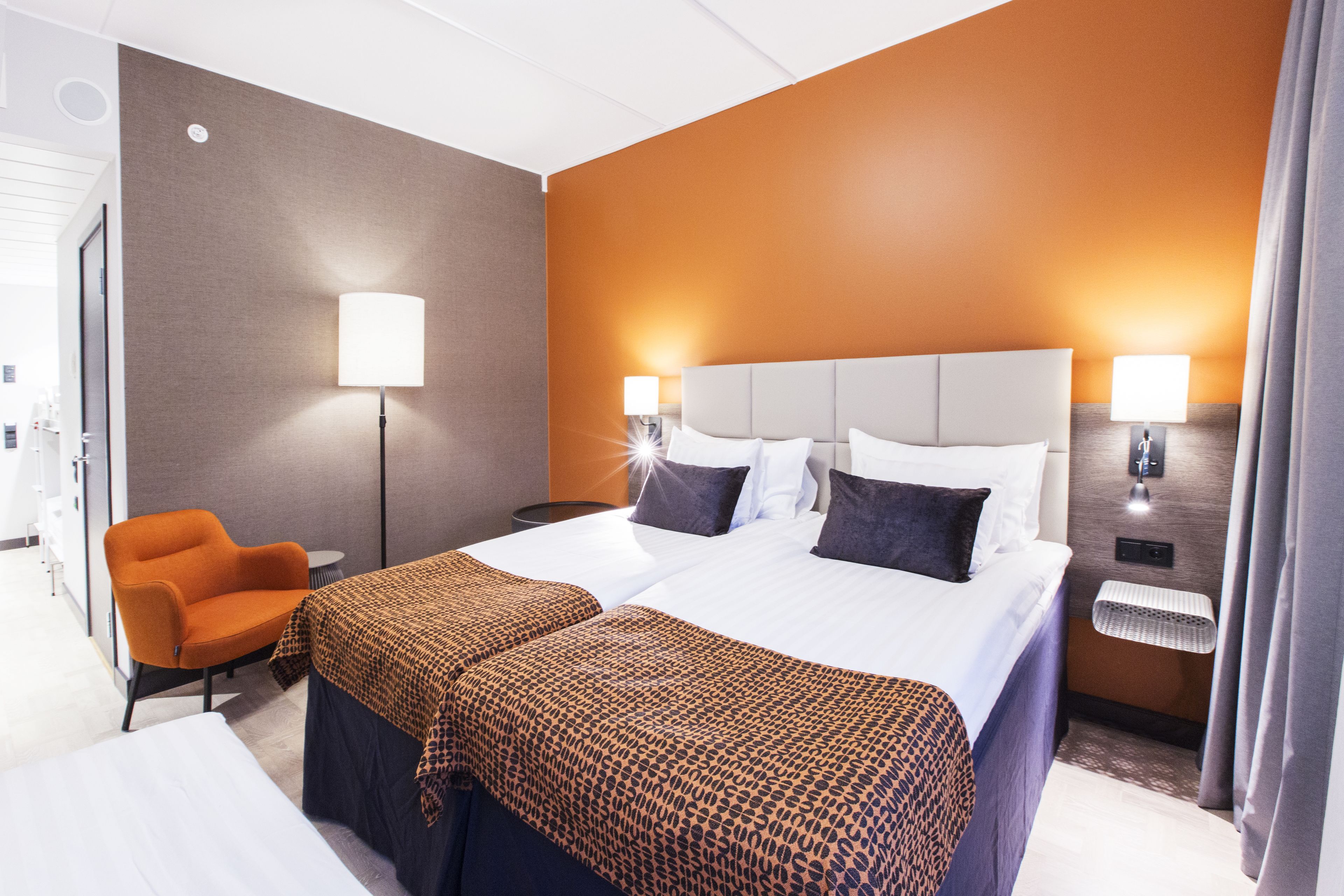 Habitación de hotel con una cama grande, dos mesitas de noche, una silla y una mesita con lámpara.