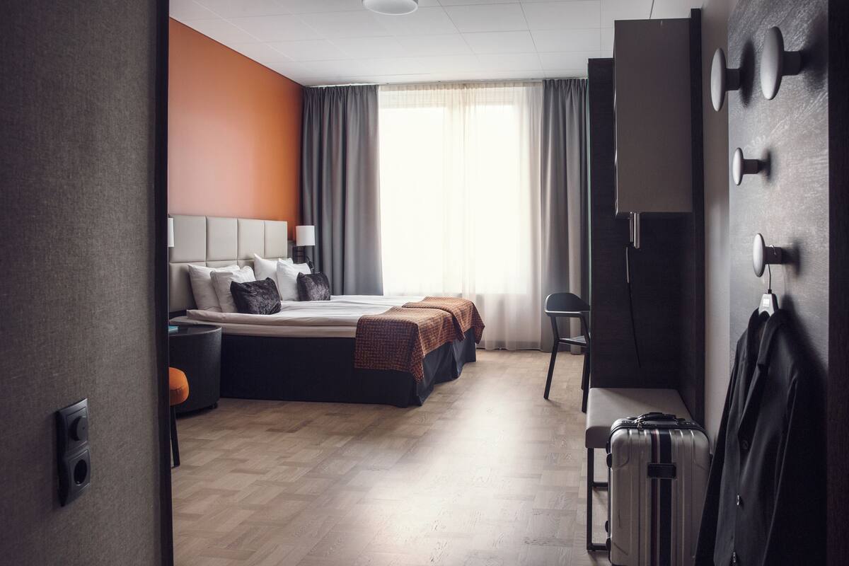 A modern hotel room with a large bed, a desk, a chair, and a suitcase.