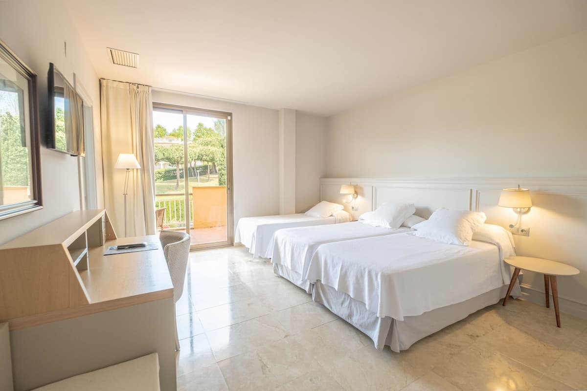 A hotel room with two beds, a desk, and a balcony.