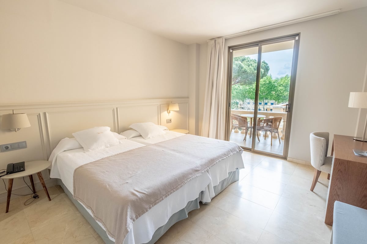 A hotel room with a large bed, a desk, and a view of the outdoors through a sliding door.