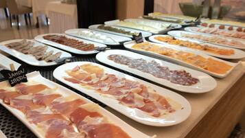 Un bufé con una variedad de alimentos, incluyendo carnes y quesos.