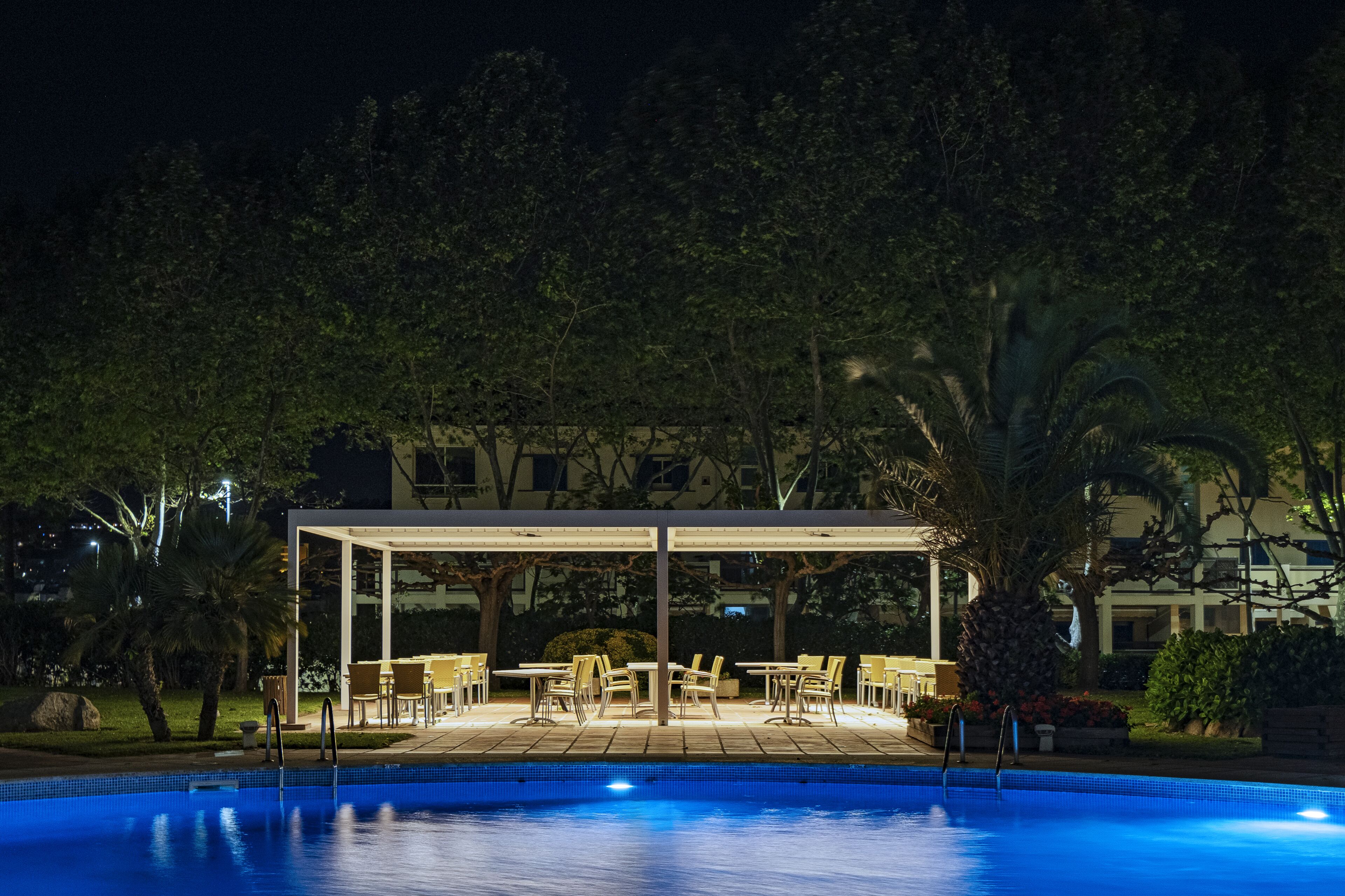Un área de piscina con una zona de estar cubierta y mobiliario exterior.