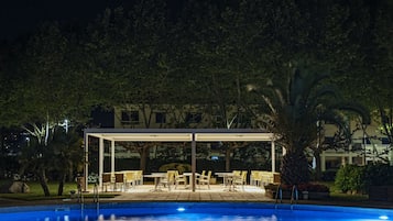 Un área de piscina con una zona de estar cubierta y mobiliario exterior.