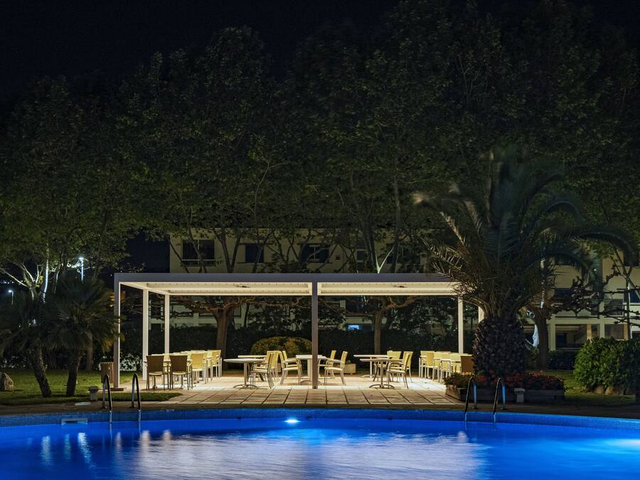 Un área de piscina con una zona de estar cubierta y mobiliario exterior.