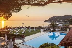 Un resort con piscina, tumbonas y vistas al mar al atardecer.