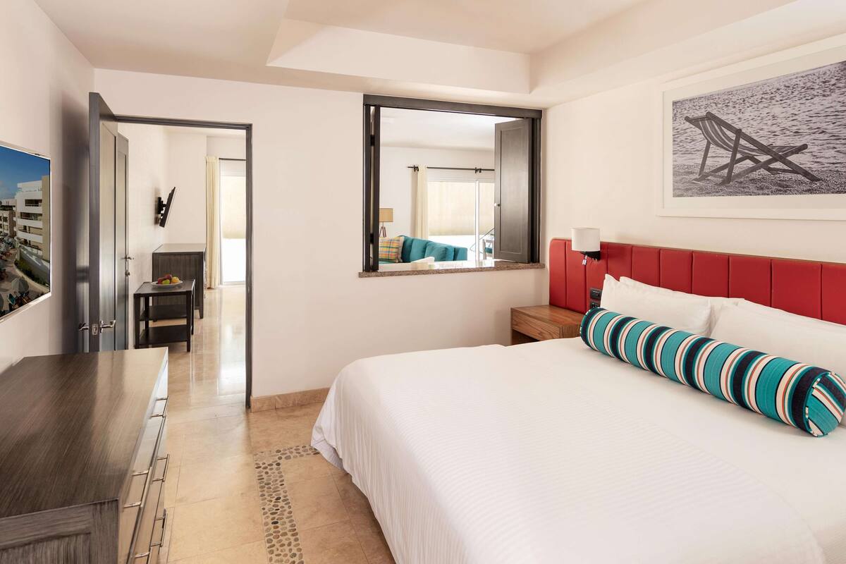 A hotel room with a bed, a desk, a chair, a mirror, and a window.