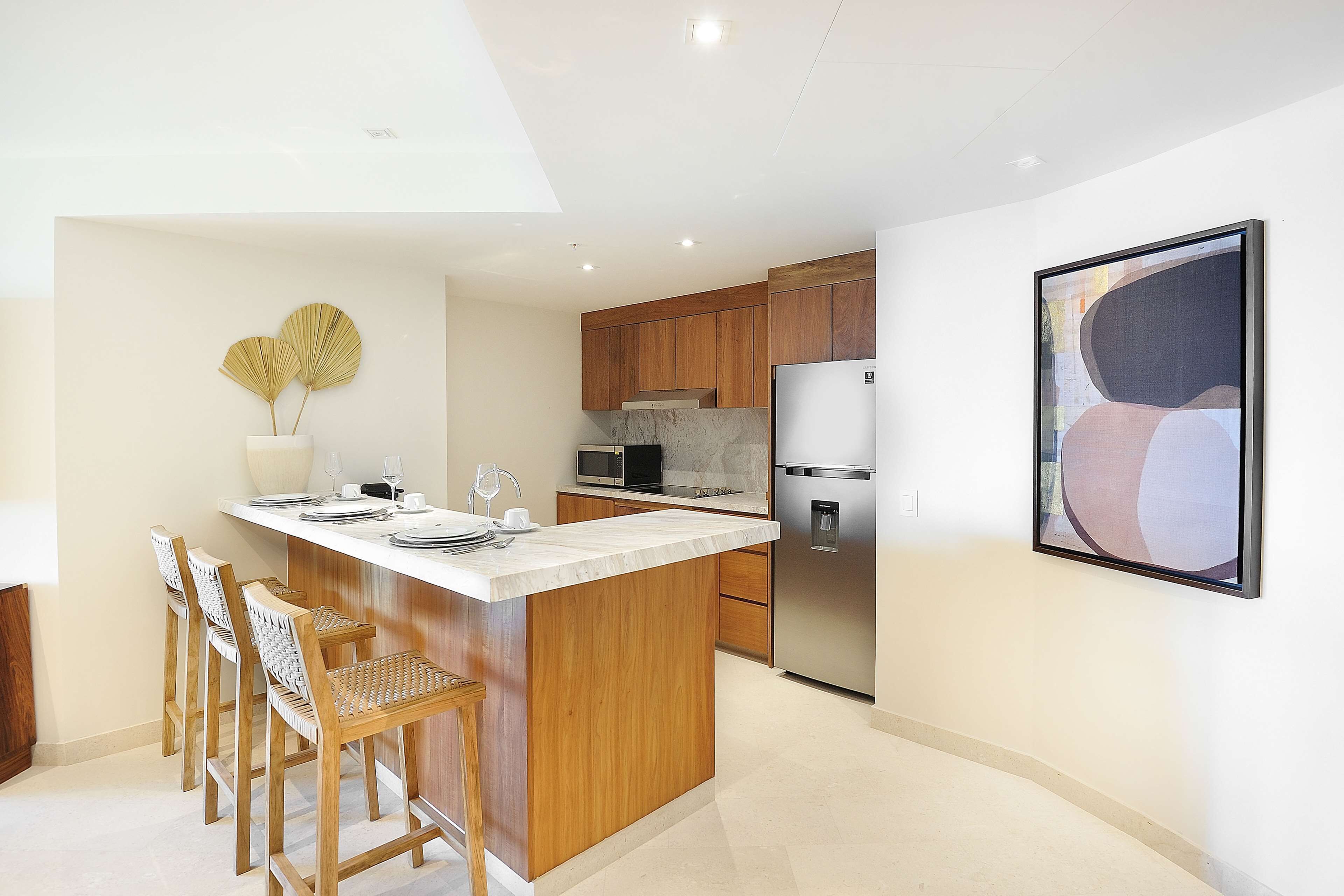 A modern kitchen with wooden cabinets, a marble countertop, and a stainless steel refrigerator.