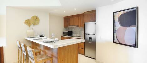 A modern kitchen with wooden cabinets, a marble countertop, and a stainless steel refrigerator.