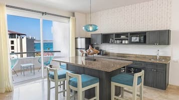 A modern kitchen with a central island, bar stools, and a view of the ocean through large sliding doors.