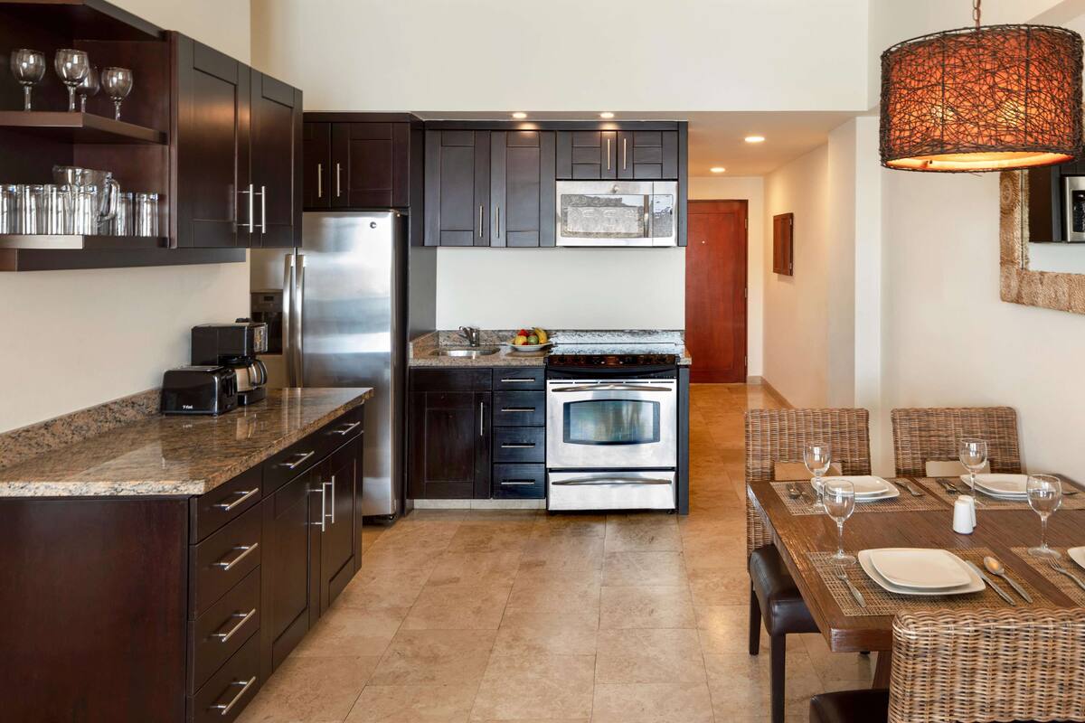 A modern kitchen with dark cabinetry, stainless steel appliances, and a dining area with wicker furniture.