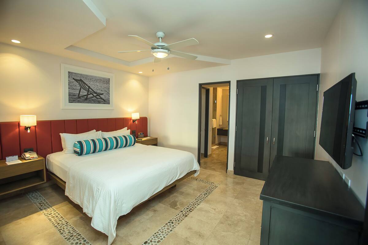 A hotel room with a bed, nightstands, a ceiling fan, a TV, and a wardrobe.