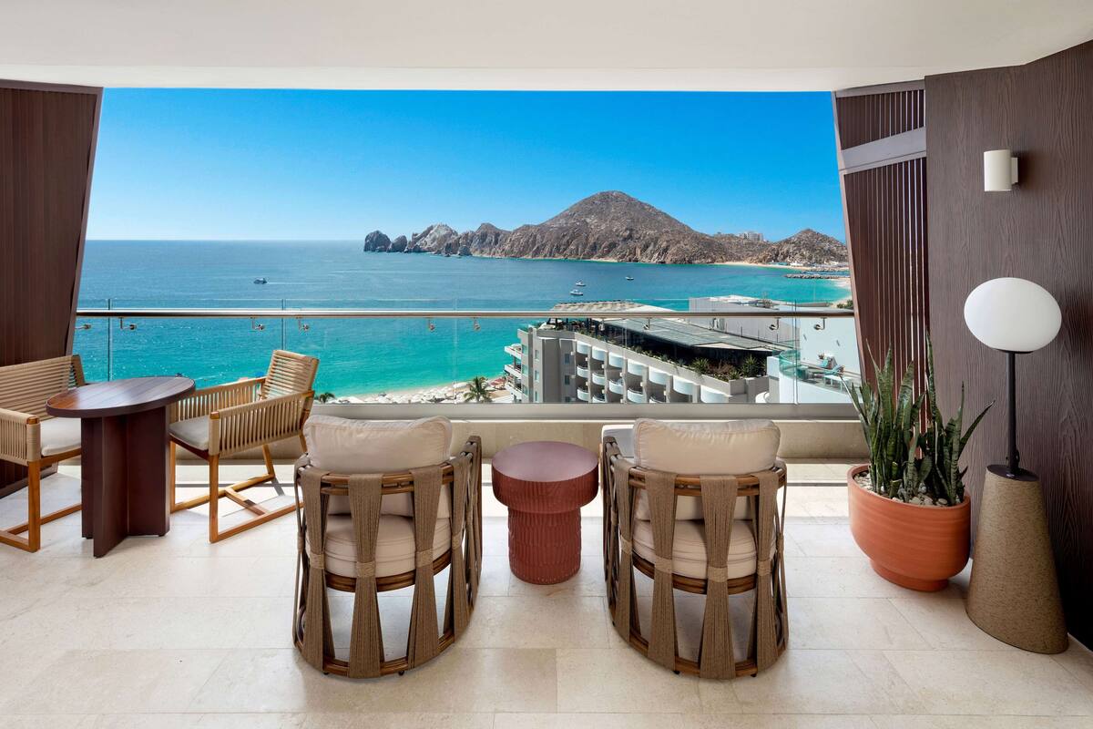 A balcony with wicker furniture, a potted plant, and a view of the sea and mountains.
