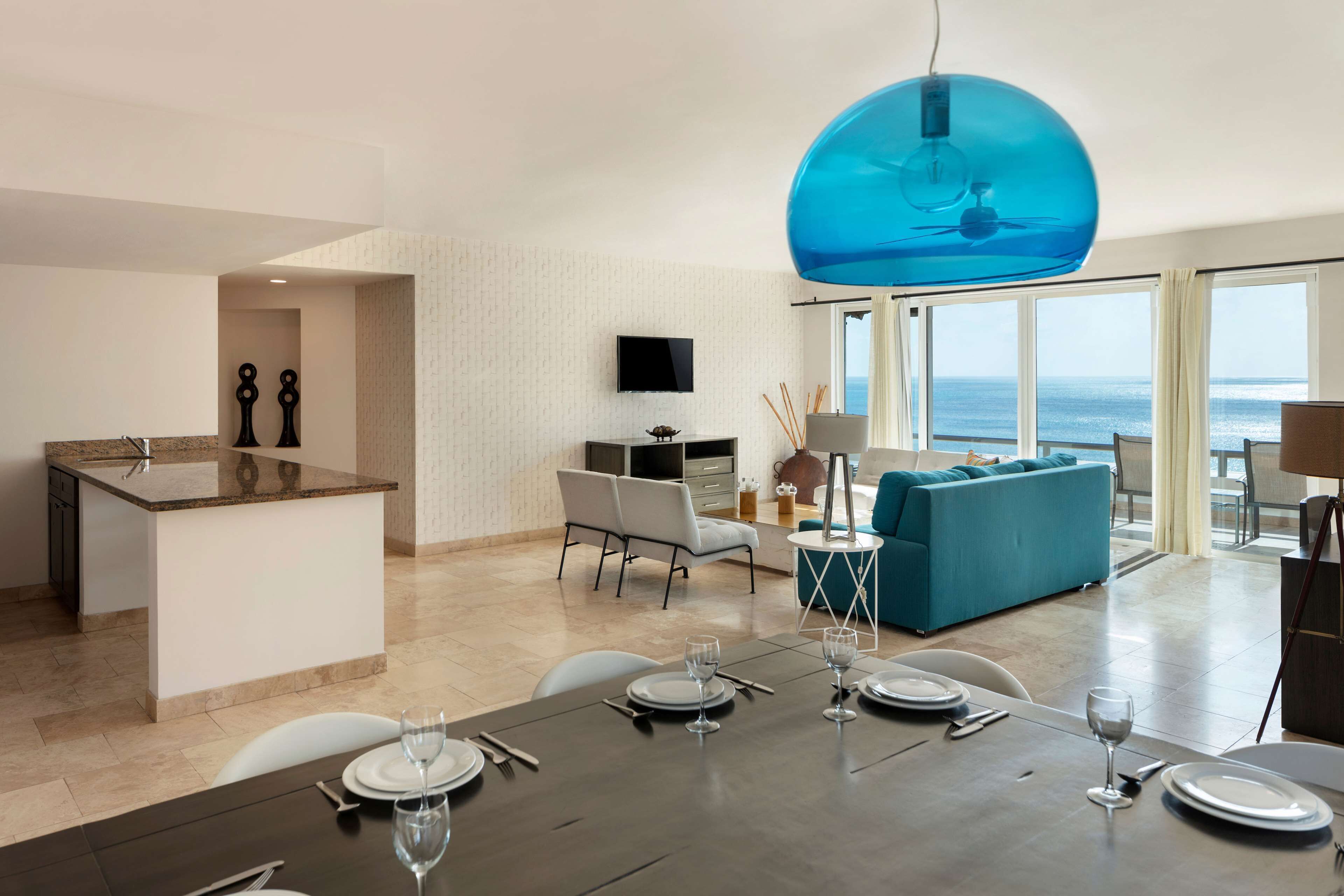 A modern living room with a large window, a blue spherical light fixture, and a dining area set for four.