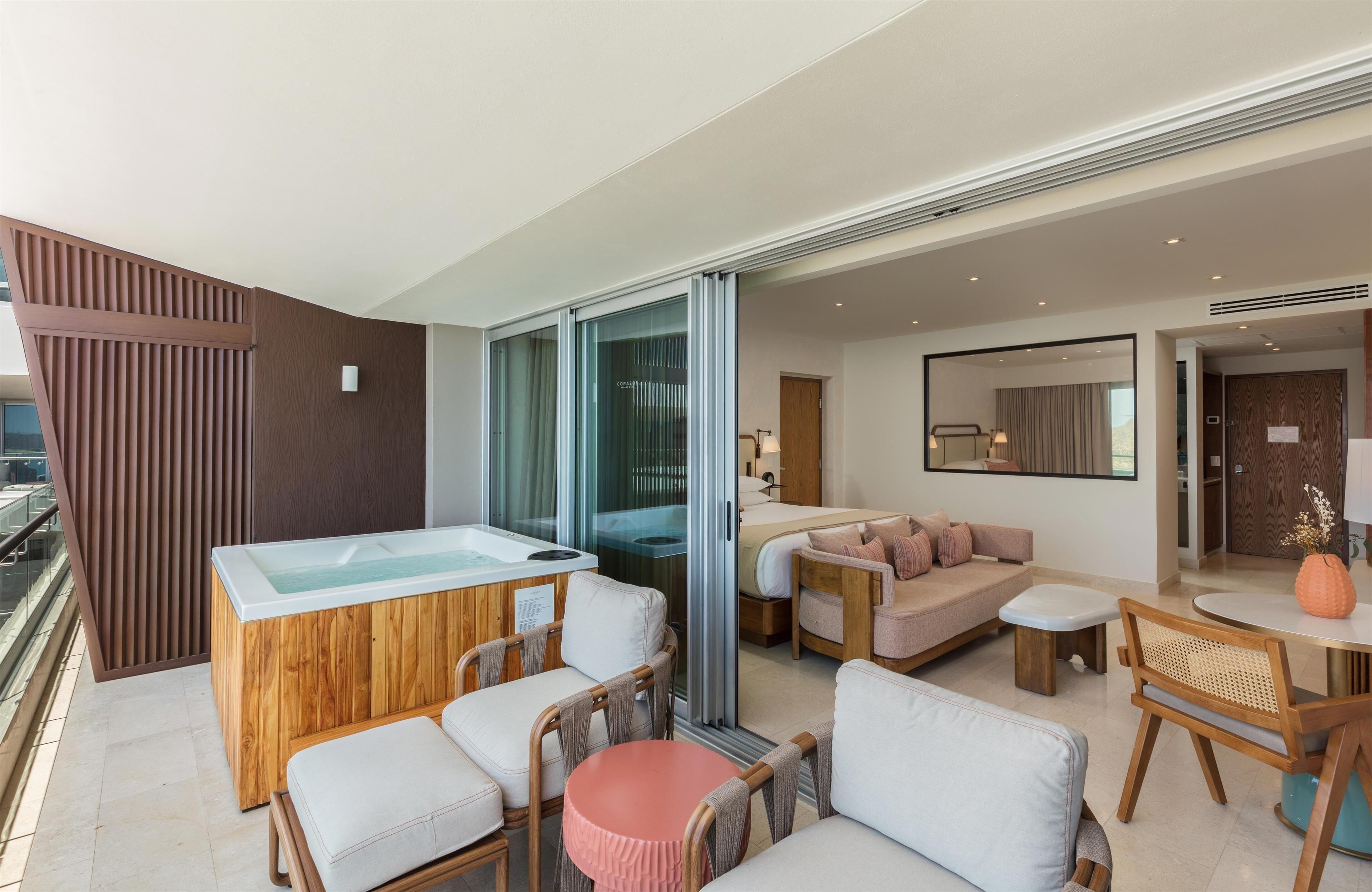 A modern hotel room with a wooden spa area, a sofa set, a dining table, and a large window.