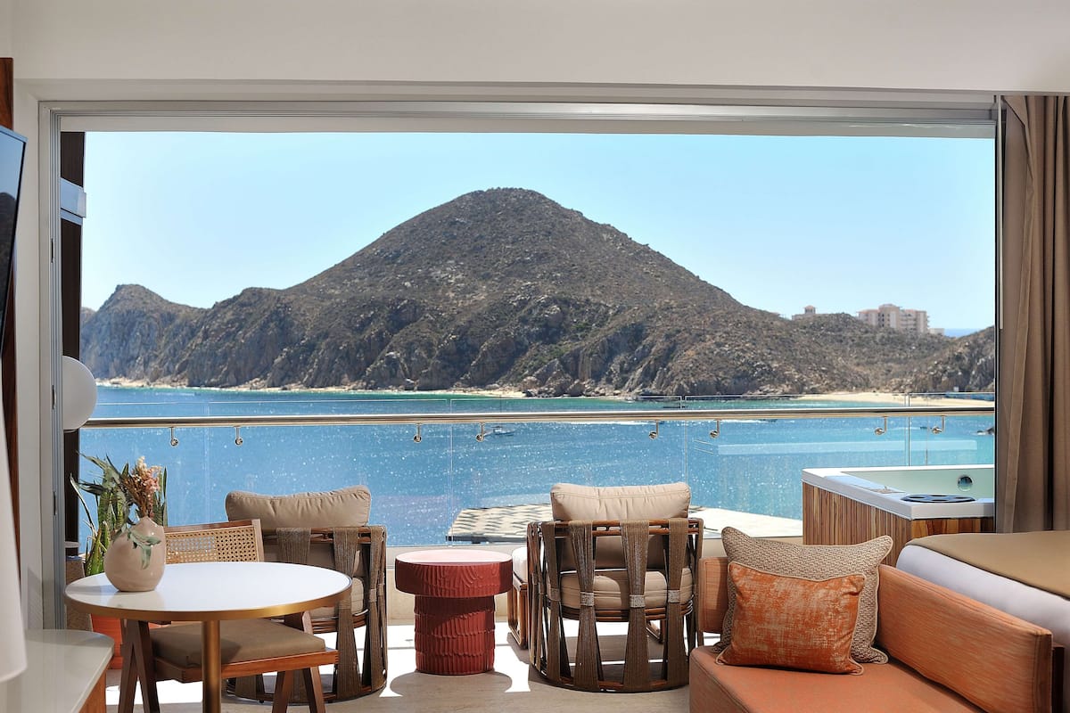 A balcony with a view of a mountain and the sea, furnished with a sofa, chairs, and a small table.