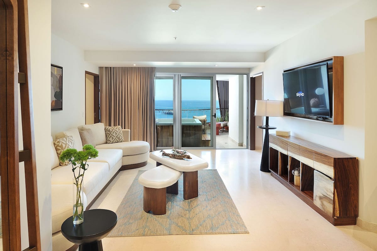 A modern living room with a sofa, a coffee table, a TV, and a view of the sea.